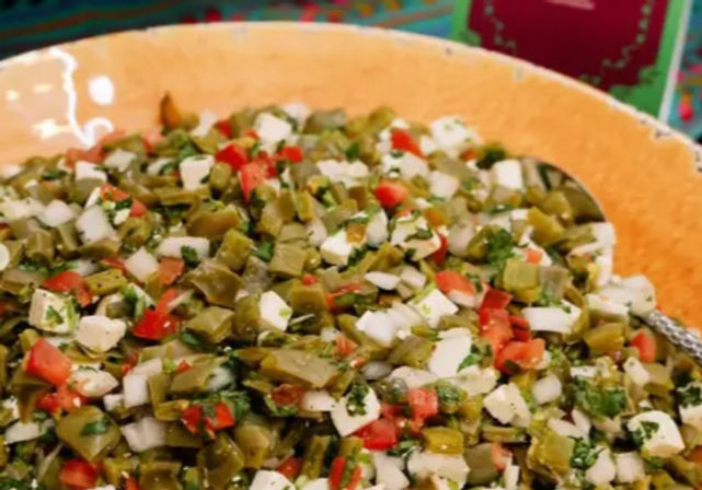 Colorful Mexican nopal (cactus) salad with diced nopales, tomatoes, white cheese, onion and cilantro in an orange serving bowl