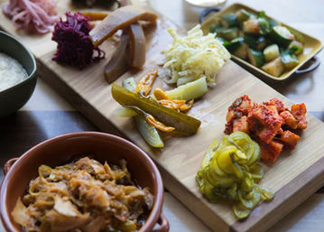 Colorful Korean banchan board with spicy kimchi, cubed radish, shredded cabbage and assorted pickled cucumbers served on a wooden platter
