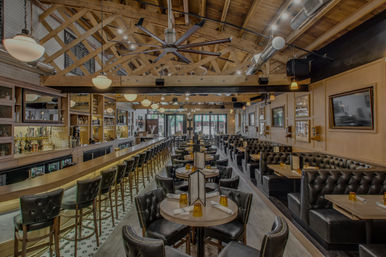 Stylish restaurant and bar interior with a long wooden bar and leather barstools, tufted booth seating, round tables, exposed wooden beams, pendant lights and industrial ductwork.