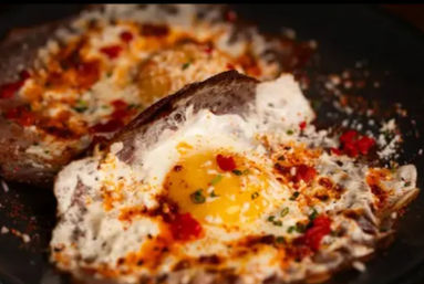 Two sunny-side-up fried eggs in a skillet with runny yolks, crispy browned edges and a sprinkle of chili flakes, paprika and chopped chives for a spicy breakfast