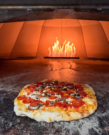 Artisan pepperoni and mushroom pizza resting on a floured stone in a blazing wood-fired oven