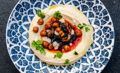 Creamy hummus swirled on a blue patterned plate topped with roasted chickpeas, a red chili oil drizzle and fresh parsley — Mediterranean mezze overhead view