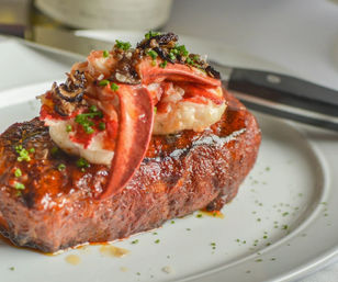 Decadent surf-and-turf: seared steak topped with lobster claw and tender lobster meat, butter glaze, chopped chives and shaved truffle on a white plate — elegant steakhouse presentation
