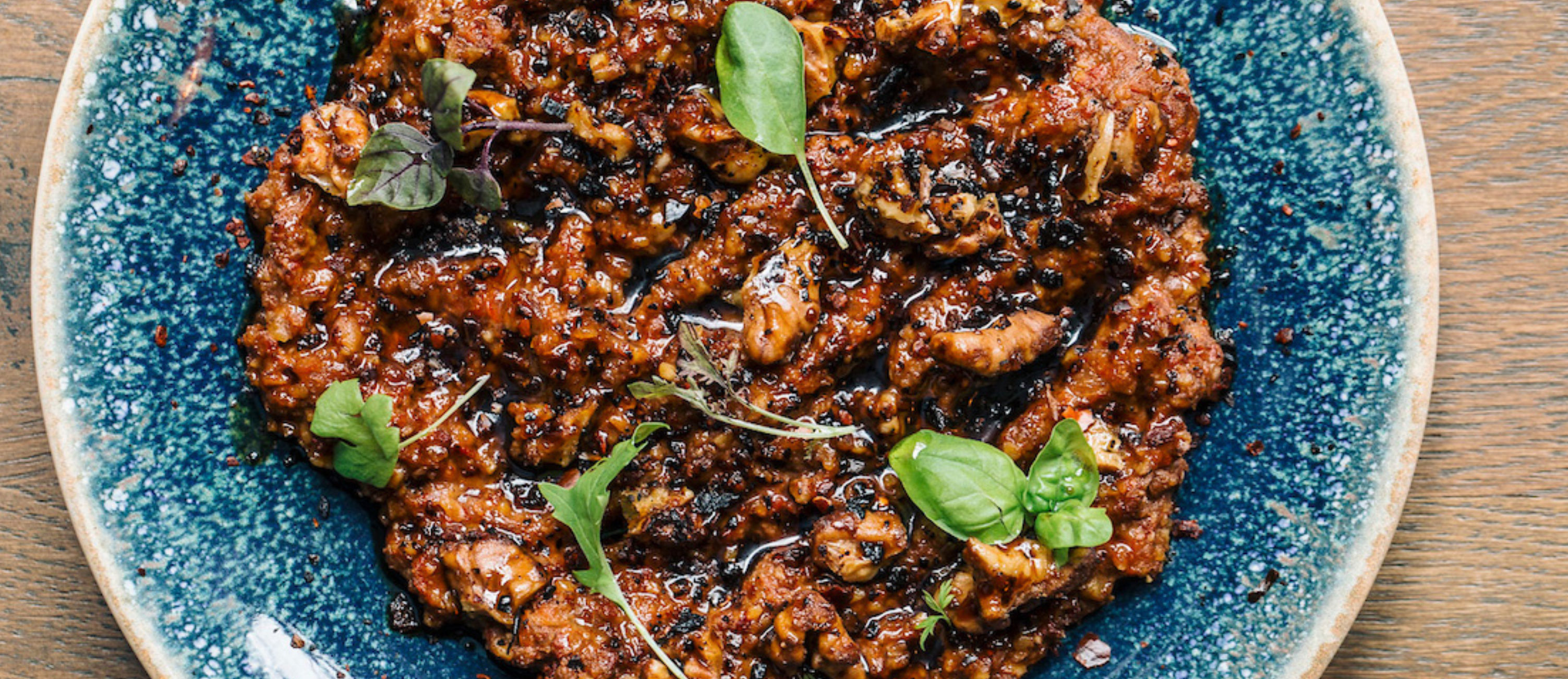 Smoky, chunky muhammara-style red pepper and walnut dip drizzled with olive oil and garnished with basil microgreens on a blue ceramic plate over a wooden table
