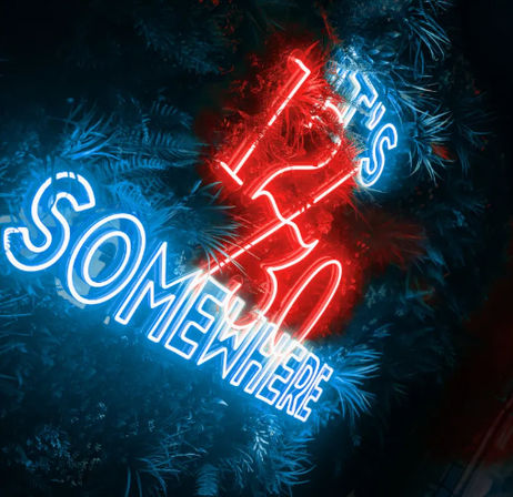 Tilted blue neon "SOMEWHERE" sign with a glowing red neon abstract symbol nestled in lush tropical foliage, moody nighttime neon decor.