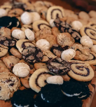 Assorted fresh-baked cookie platter on a wooden board — chocolate pinwheels, powdered snowball cookies, chocolate crinkles and cream sandwich cookies