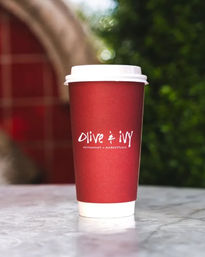 Red takeaway coffee cup with white lid on a marble table, outdoor cafe setting with blurred green foliage and tiled background