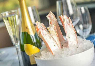 Chilled king crab legs on crushed ice in a white bowl with a lemon wedge, champagne bottle and flutes in an elegant seafood dining scene