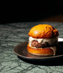 Juicy gourmet cheeseburger with melted cheese on a glossy brioche bun, served on a black plate on a green marble tabletop