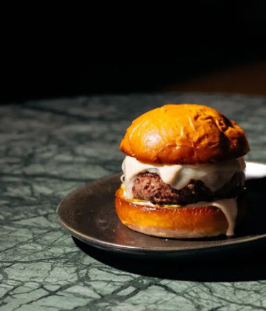 Juicy gourmet cheeseburger with melted cheese on a glossy brioche bun, served on a black plate on a green marble tabletop