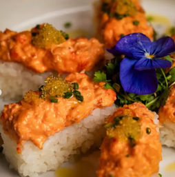 Spicy crab nigiri: rectangular sushi rice topped with creamy orange crab mix, golden tobiko, microgreens and a bright purple edible flower