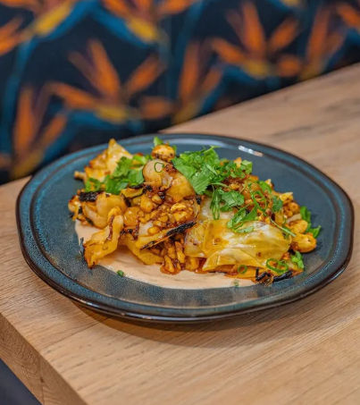 Restaurant-style plate of charred corn and cabbage topped with fresh cilantro and scallions on a dark ceramic plate, photographed on a wooden table.