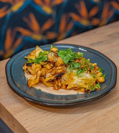 Restaurant-style plate of charred corn and cabbage topped with fresh cilantro and scallions on a dark ceramic plate, photographed on a wooden table.