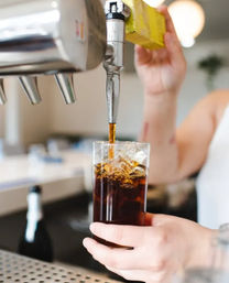Hand pouring draft cold brew coffee from a tap into a tall glass filled with ice at a cafe counter
