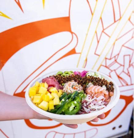 Hand holding a vibrant poke bowl by a food truck: sushi-grade salmon and tuna, diced mango, jalapeño slices, edamame, shredded cabbage, pickled ginger and crunchy quinoa topping.