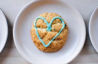 Overhead shot of a round funfetti-style cookie decorated with a bright blue heart icing on a white plate