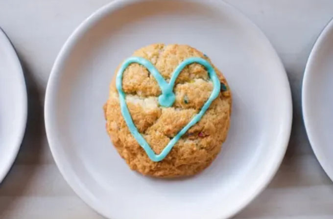 Overhead shot of a round funfetti-style cookie decorated with a bright blue heart icing on a white plate