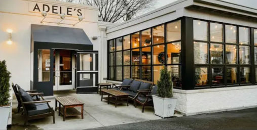 Cozy modern cafe exterior with a black awning, large black-framed windows, and outdoor lounge seating on a concrete patio