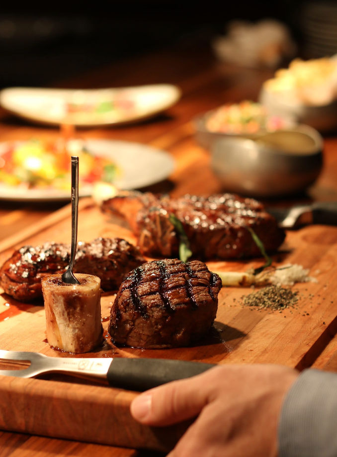 Juicy grilled filet mignon medallion with crosshatch grill marks and roasted bone marrow with a spoon on a wooden cutting board — gourmet steakhouse dinner.