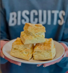 Golden flaky layered biscuits stacked on a white plate held in hands — buttery Southern-style breakfast pastry