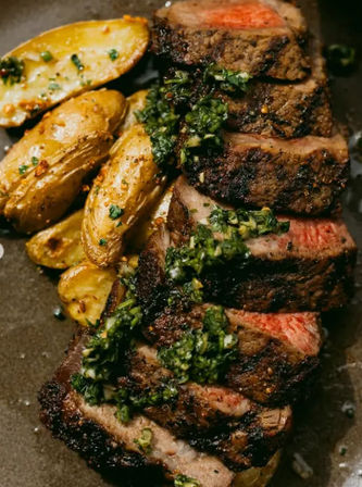 Juicy sliced grilled steak topped with chimichurri sauce served with roasted fingerling potatoes on a rustic plate