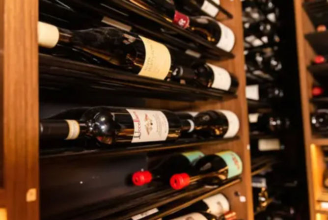 Assorted wine bottles stored horizontally on wooden racks in a cellar-style display, with visible labels and red bottle caps.