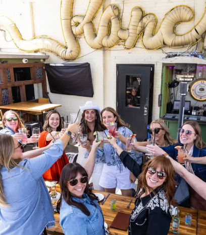 Smiling group of friends raising cocktails for a brunch toast on a sunny urban outdoor patio