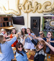Smiling group of friends raising cocktails for a brunch toast on a sunny urban outdoor patio