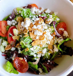 Crisp mixed greens salad with cherry tomatoes, crumbled feta, toasted almond slices and diced cucumber in a white bowl — bright healthy lunch