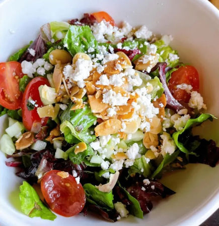 Crisp mixed greens salad with cherry tomatoes, crumbled feta, toasted almond slices and diced cucumber in a white bowl — bright healthy lunch