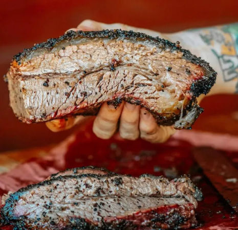 Close-up of a juicy Texas-style smoked brisket slice with dark peppery bark and pink smoke ring, held over a cutting board