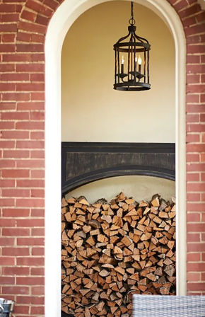 Red brick arched doorway revealing a porch nook with neatly stacked firewood and a rustic black hanging lantern against a beige wall
