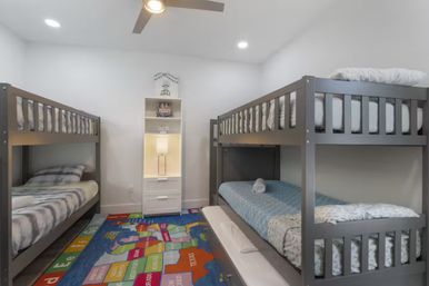 Bright kids' shared bedroom with two gray bunk beds, white shelf and lamp, colorful U.S. map rug and ceiling fan