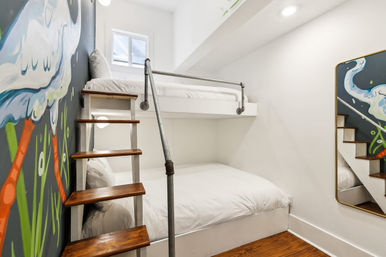 Cozy two-level bunk bed with white bedding and wooden ladder in a compact modern bedroom, colorful mural of a bird and grass on the wall and a full-length mirror reflecting the stairs.