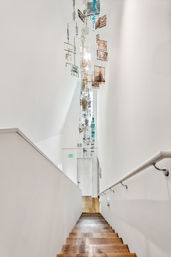 Bright modern stairwell with wooden steps and white walls, featuring a tall hanging glass mobile art chandelier with colorful panels