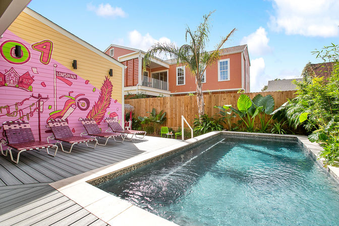 Sunny backyard plunge pool with turquoise water, pink Louisiana mural, palm tree and lounge chairs