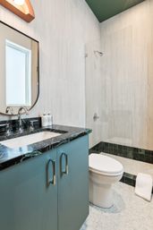 Modern bathroom with teal vanity, black marble countertop, chrome faucet, glass walk-in shower and white tiled walls, bright clean design.