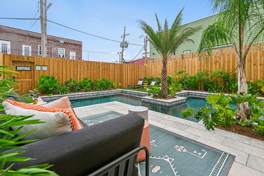 Private urban backyard pool with palm trees, lush tropical landscaping, modern lounge seating and tiled patio beside a rectangular plunge pool enclosed by a wooden fence.