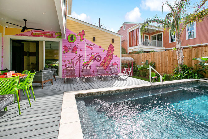 Vibrant backyard pool and gray deck with lime-green dining chairs, lounge chairs, palm tree and a playful Louisiana-themed mural.