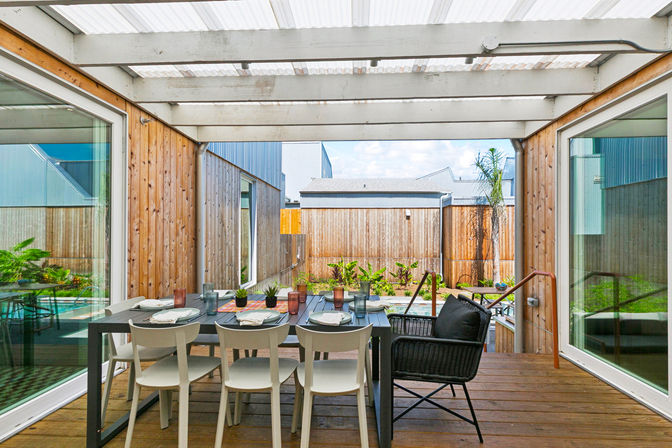 Covered timber-clad backyard courtyard with a modern outdoor dining table set for six, potted plants, glass sliding doors and a small plunge pool beyond