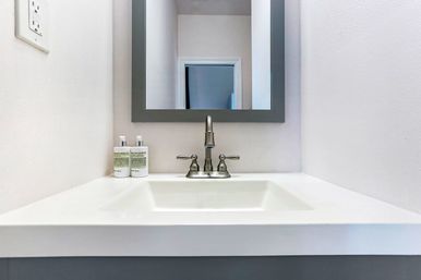 Minimalist white bathroom sink with stainless faucet, gray-framed mirror, and two soap dispensers on a white vanity in a modern powder room