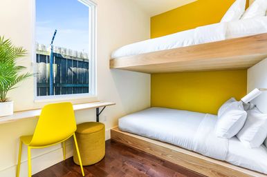 Bright modern small bedroom with built-in wooden bunk beds, yellow accent wall, crisp white linens, compact window-side desk with yellow chair and potted plant.