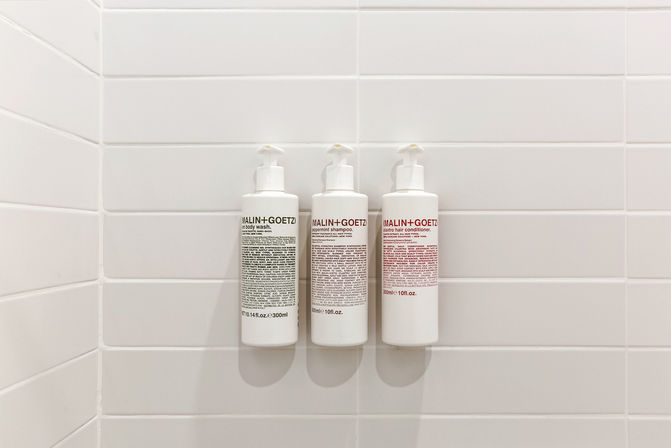 Three white pump dispensers (shampoo, conditioner, body wash) wall-mounted on a white subway-tile shower — minimalist bathroom amenity setup.