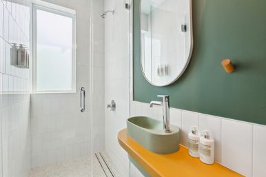 Stylish contemporary bathroom with green accent wall, oval mirror, yellow countertop, green vessel sink and glass walk-in shower with frosted window.