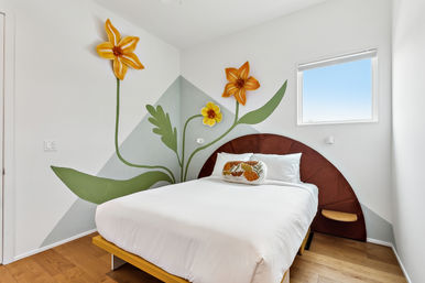 Bright modern bedroom with white bedding, wooden floor, curved rust headboard and large yellow flower wall mural with a decorative floral pillow