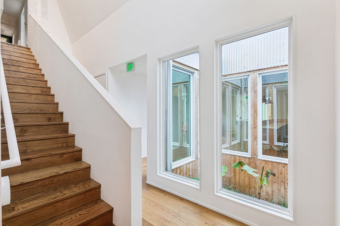 Bright modern interior with oak staircase, white walls and tall windows overlooking a small enclosed courtyard