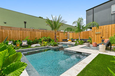 Sunny modern backyard oasis with rectangular swimming pool and raised spa, palm trees and tropical plants, wooden privacy fence and contemporary outdoor lounge seating.