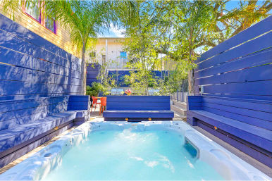 Sunny residential courtyard with bubbling outdoor hot tub, blue wooden benches and privacy fence, palm trees and cozy backyard patio seating