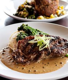 Sizzling grilled steak on a white plate with creamy peppercorn sauce, whipped mashed potatoes, broccolini and thin green onion strips — upscale restaurant entrée.