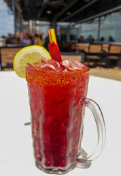 Zesty red Mexican-style cocktail in a frosted mug with chili-salt rim, crushed ice, lime wheel and candy straw on a sunny outdoor patio